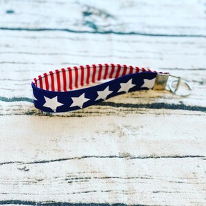 May include: A red, white, and blue fabric key chain with white stars on a blue background. The key chain has a silver key ring.