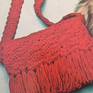 May include: A red crocheted shoulder bag with a fringe trim. The bag is made with a simple stitch pattern and has a long strap.