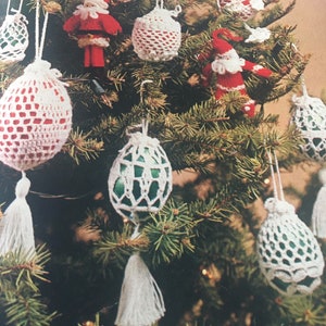 May include: A Christmas tree decorated with crocheted ornaments. The ornaments are white, green, and red and have a tassel hanging from the bottom. There are also two crocheted Santa Claus figures on the tree.
