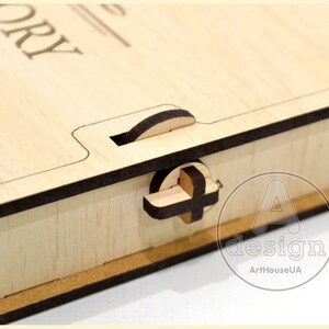 May include: A wooden box with a latch and the word "STORY" engraved on the top. The box is made of light wood with a dark brown trim. The box is closed and the latch is in the closed position.