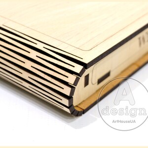 May include: A wooden box with a decorative, layered design on the front. The box is made of light wood and has a dark brown trim.