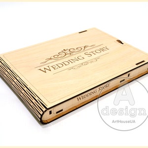 May include: A wooden box with a hinged lid, engraved with the words "Wedding Story" in a decorative font. The box has a detailed design on the spine.