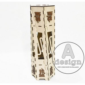 May include: A wooden bottle holder with a geometric design. The holder is made of light brown wood and has a decorative pattern on the front. The holder is designed to hold a single bottle of wine or liquor.