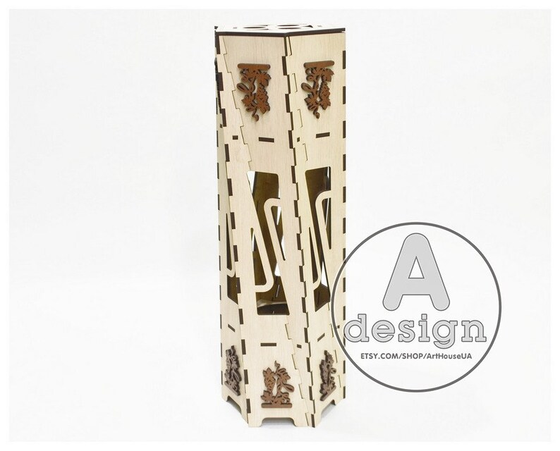 May include: A wooden bottle holder with a geometric design. The holder is made of light brown wood and has a decorative pattern on the front. The holder is designed to hold a single bottle of wine or liquor.