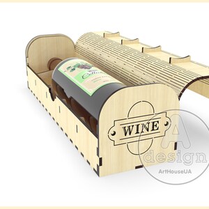 Puede incluir: Una caja de madera para vino con una tapa con bisagras y un hueco para una botella de vino. La caja est&aacute; hecha de madera clara y tiene una etiqueta "WINE" en la parte delantera.