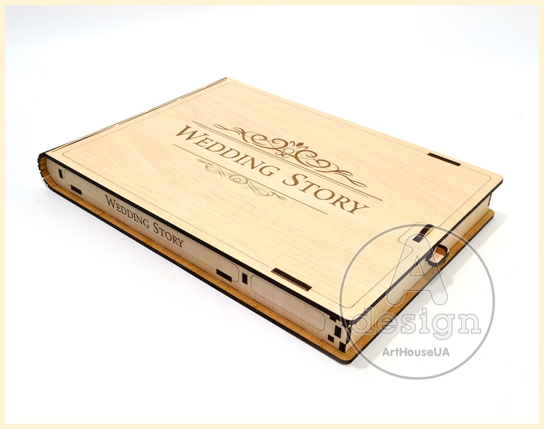 May include: A wooden box with a hinged lid, engraved with the words "Wedding Story" and a decorative scroll design. The box is made of light wood and has a natural finish.