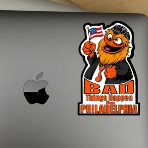 Könnte beinhalten: Ein Aufkleber mit einer Comicfigur mit orangefarbenem Fell, die einen schwarzen Anzug trägt und eine amerikanische Flagge hält. Der Text auf dem Aufkleber lautet "Bad Things Happen in Philadelphia".