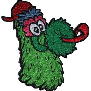 May include: Green and red embroidered patch of a cartoon character wearing a red baseball cap. The character has large eyes and a long green tongue sticking out.