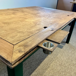 May include: A rectangular wooden table with a natural wood grain top and dark green legs. The table features a recessed centre section, a wide wooden border, and extendable side shelves equipped with integrated stainless steel cup holders.