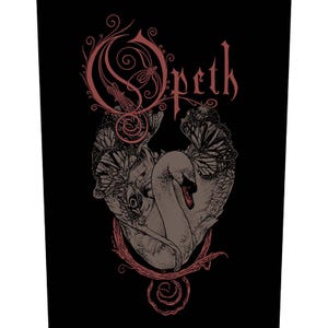 May include: Black graphic with the band name "Opeth" in reddish-brown lettering. The design features a swan with butterfly wings and floral details. The artwork has a gothic or metal aesthetic, set against a black background.