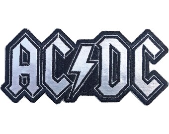 May include: A silver and black embroidered patch with the word "AC/DC" in a bold, stylised font.