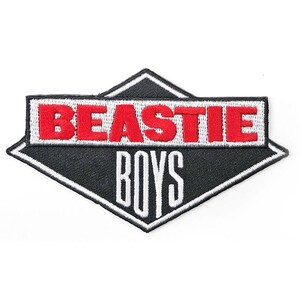 May include: An embroidered patch featuring the words "BEASTIE BOYS" in red and white. The patch is black with a white diamond border. Suitable for clothing or accessories.
