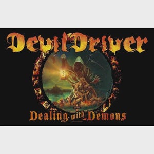 Puede incluir: Camiseta negra con el nombre de la banda "DevilDriver" en letras góticas naranjas y amarillas. La imagen incluye un gráfico circular de una figura encapuchada sosteniendo una linterna, con el texto "Dealing with Demons" debajo.