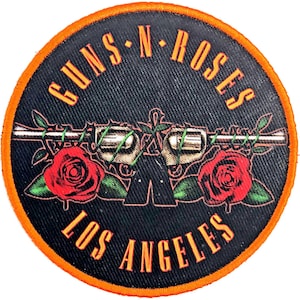 May include: A black and orange circular patch with the text "Guns N' Roses Los Angeles" in white. The patch features a stylised image of a gun with roses on either side.