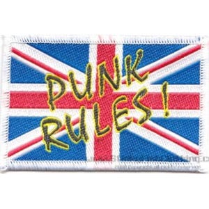 Puede incluir: Parche bordado rectangular con el diseño de la bandera de la Union Jack y las palabras "PUNK RULES!" en letras amarillas y negras. El parche tiene un borde blanco. El diseño de la bandera incluye los colores rojo, blanco y azul.