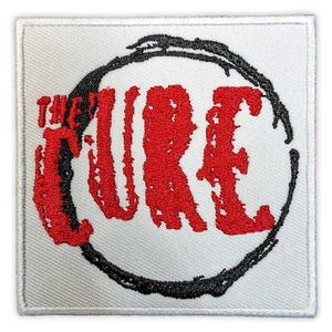 May include: Embroidered patch featuring the band name "THE CURE" in bold red letters. The text is inside a black, uneven circle on a white square background. The patch has a white border.