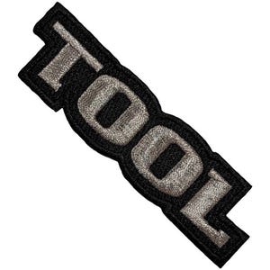 May include: Embroidered patch with the word "TOOL" in silver thread on a black backing. The patch is rectangular with rounded edges. The letters are bold and easy to read, suitable for application on clothing or accessories.