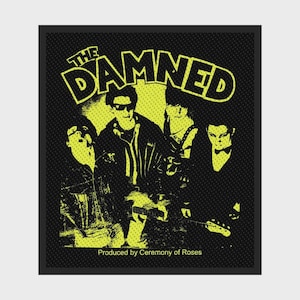 May include: A black and yellow patch featuring the band "The Damned." The image shows a stylized illustration of the band members. The text "THE DAMNED" is in large, bold, yellow letters above the band members. The text "Produced by Ceremony of Roses" is at the bottom.