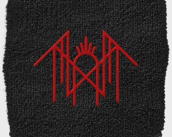 Puede incluir: Muñequera negra con un diseño bordado en rojo. El diseño presenta una forma estilizada de sol o corona con líneas verticales y elementos angulares. La muñequera está hecha de un material texturizado y absorbente.