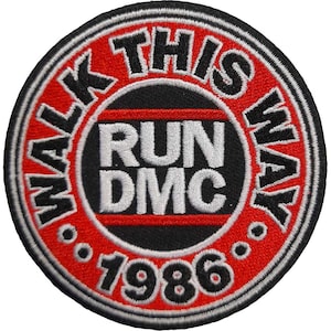 May include: Round embroidered patch with a black border. The text "WALK THIS WAY" in white encircles a central black circle with "RUN DMC" and "1986" in white. The background is red.