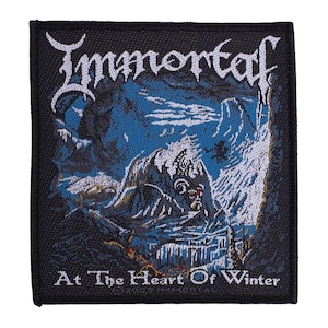 Peut inclure: Écusson carré noir avec le nom du groupe "Immortal" en lettres gothiques blanches au-dessus d'une scène de paysage hivernal bleu et blanc. Le texte "At The Heart Of Winter" est en dessous.