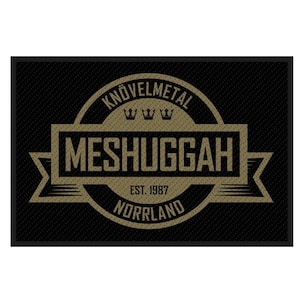 May include: Black rectangular doormat with a textured surface. The doormat features a gold and black design with the text "KNÖVELMETAL" above "MESHUGGAH" and "EST. 1987 NORRLAND". The design includes three crowns.
