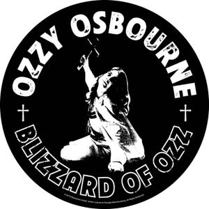 Peut inclure: Autocollant circulaire noir et blanc avec Ozzy Osbourne. Le texte "OZZY OSBOURNE" et "BLIZZARD OF OZZ" est en blanc, en gras, autour de l'image d'Osbourne. Une croix est de chaque côté du texte.