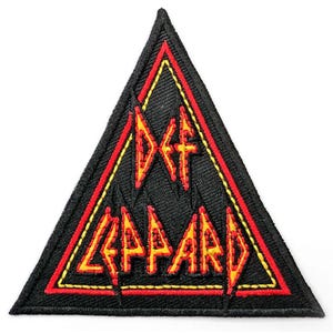 May include: A triangular embroidered patch featuring a black background with a red and yellow border. The text DEF LEPPARD is stitched in red and yellow lettering in the centre of the triangle, with a jagged, stylised font design.