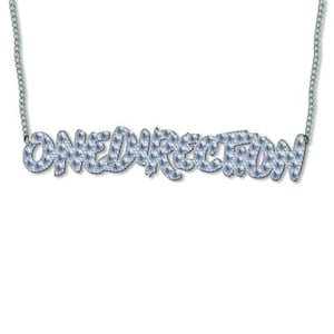May include: A silver necklace spelling out "ONEDIRECTION" in a light blue, sparkling font. The letters are filled with a pattern of small, blue crystals. The necklace is suspended from a fine silver chain.
