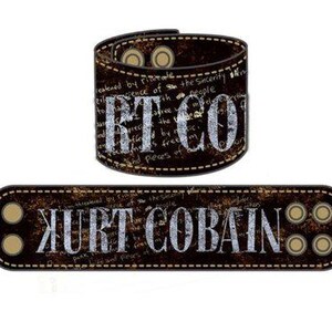Puede incluir: Brazalete de cuero marrón y pulsera rectangular con el texto "RT CO" y "KURT COBAIN" en blanco. Las pulseras tienen un aspecto envejecido y vintage con remaches metálicos y costuras blancas.