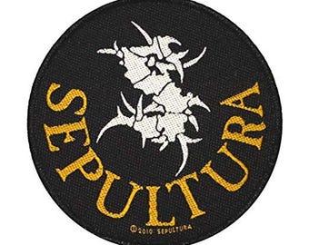 May include: A round black patch featuring the word "SEPULTURA" in gold, arched around the top and bottom. A white, abstract design is in the center. The text "©2010 SEPULTURA" is at the bottom.