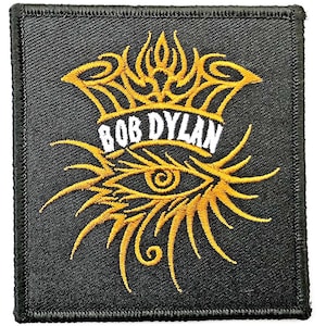 May include: Black square patch featuring the text "BOB DYLAN" in white, beneath a gold crown design. Below the text is a gold eye design with radiating lines. The patch has a black border.