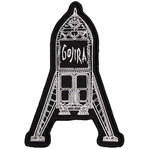 May include: Black and white embroidered patch featuring the word "GOJIRA" in a stylized font within a detailed architectural design. The patch has a unique shape, resembling a stylized letter "A" with intricate white stitching.