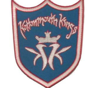 May include: A shield-shaped patch with a blue background, white and red trim, and the text "Kettemouth Kings" in white script. The patch features a white crown and stylized white "KK" design.