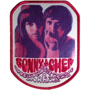 Può includere: Toppa ricamata con un'immagine rosa e viola di Sonny & Cher. La toppa ha uno sfondo bianco con il testo "SONNY & CHER" e "WESTBURY MUSIC FAIR MAR.3.68" in lettere rosa. La toppa ha un bordo rosa.