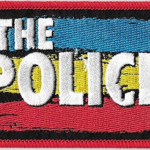 Puede incluir: Parche bordado con el texto "THE POLICE" en blanco, sobre un fondo negro. El diseño incorpora franjas horizontales azules, amarillas y rojas. El parche tiene un borde rojo, adecuado para ropa o accesorios.