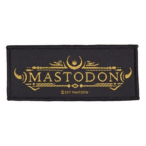 May include: Black rectangular patch with gold embroidered text and design. The word "MASTODON" is prominently displayed, with decorative elements above and below. The text "© 2017 MASTODON" is at the bottom.