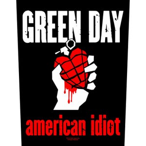 以下が含まれることがあります： 黒いグラフィック。上部に白い文字でバンド名「GREEN DAY」と表示。その下に、赤いハート型の手榴弾を持つ白い手。下部には赤い文字で「american idiot」と書かれています。大胆なグラフィックデザイン。