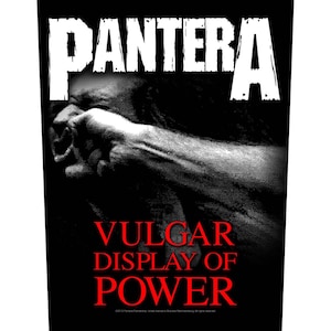 Puede incluir: Gráfico en blanco y negro con el nombre de la banda "PANTERA" en letras blancas. Debajo, una imagen en escala de grises de un puño golpeando una cara. Las palabras "VULGAR DISPLAY OF POWER" están en rojo.