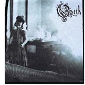 以下が含まれることがあります： スタイリッシュなフォントでバンド名「Opeth」をあしらった白黒のパッチ。パッチには、テーブルの近くにドレスを着た人のヴィンテージ写真が写っています。画像は黒い縁で囲まれています。