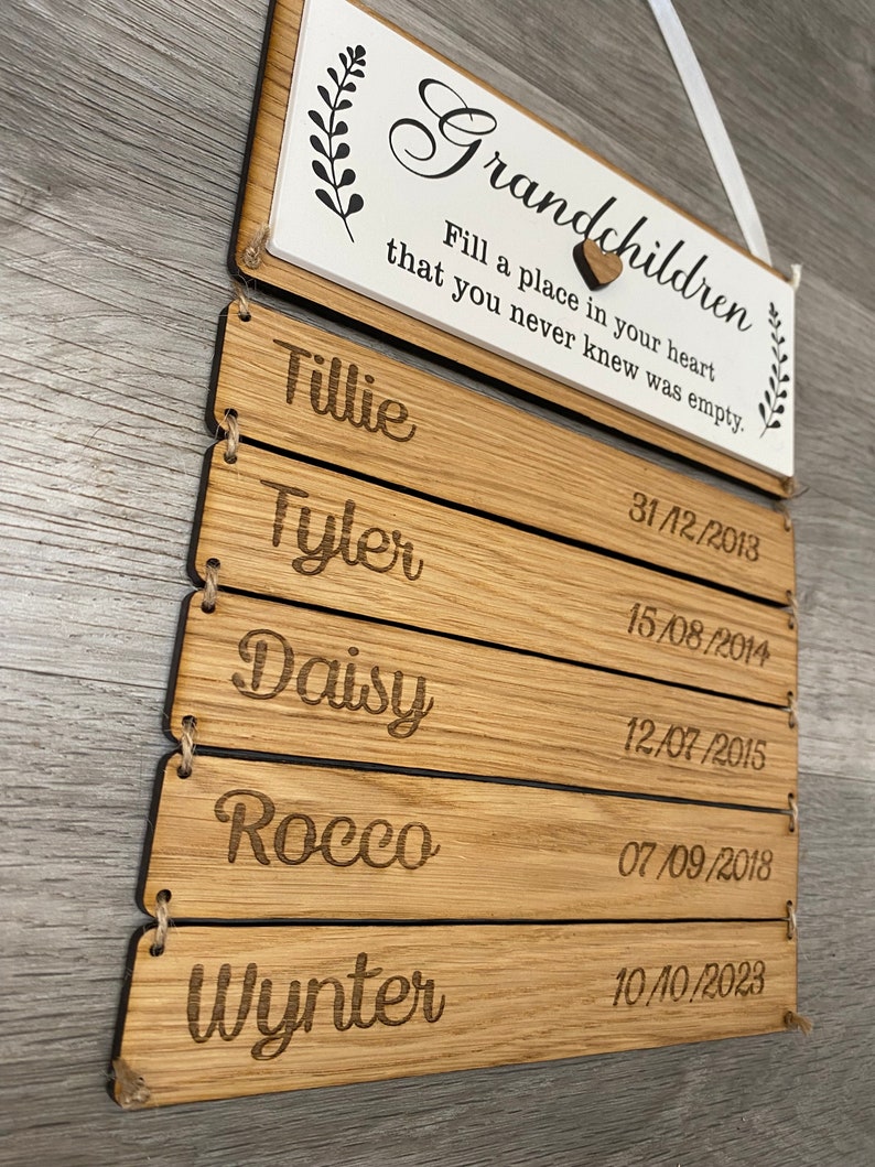 May include: Wooden sign with the text "Grandchildren Fill a place in your heart that you never knew was empty."  The sign has five wooden slats with names and dates engraved on each slat. The names are Tillie, Tyler, Daisy, Rocco, and Wynter. The dates are 31/12/2013, 15/08/2014, 12/07/2015, 07/09/2018, and 10/10/2023.
