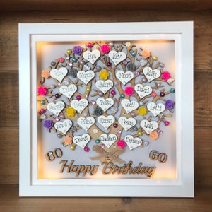 May include: A white framed illuminated box with a wooden tree design. The tree is decorated with hearts, flowers, and rhinestones. The hearts have names written on them. The box also has the words "60 Happy Birthday 60" written on it.