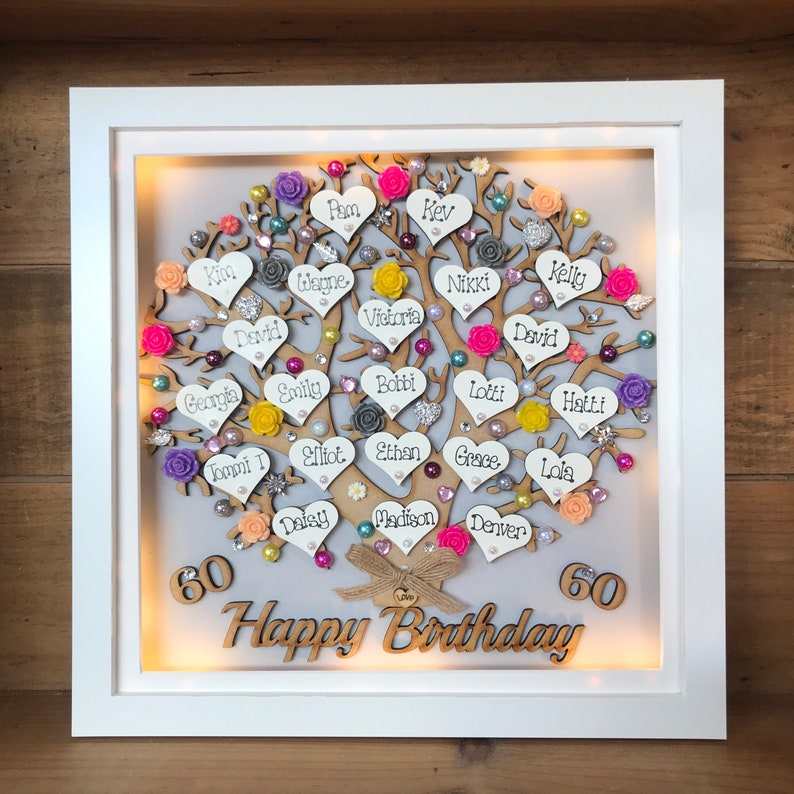 May include: A white framed illuminated box with a wooden tree design. The tree is decorated with hearts, flowers, and rhinestones. The hearts have names written on them. The box also has the words "60 Happy Birthday 60" written on it.