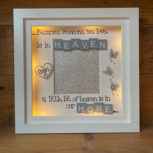 May include: A white picture frame with a silver glitter background and a photo opening. The frame has a light inside and the words "...Because someone we love. is in HEAVEN Gran a little bit of heaven is in our HOME..." are written on the frame.