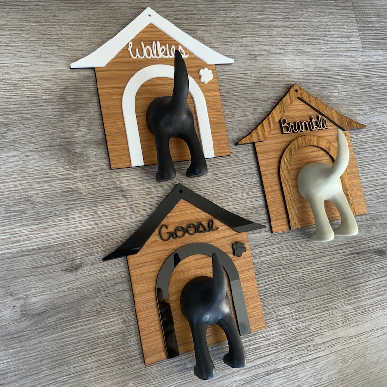 May include: Three wooden dog house shaped hooks with black and white dog silhouettes. The hooks are labeled "Walkies", "Bramble", and "Goose".