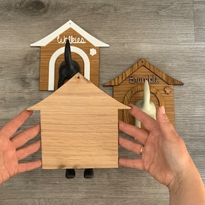 May include: Three wooden dog leash holders, each shaped like a dog house. The top house is white with the word "Winkies" written on it. The middle house is unfinished wood. The bottom house is brown with the word "Bramble" written on it.