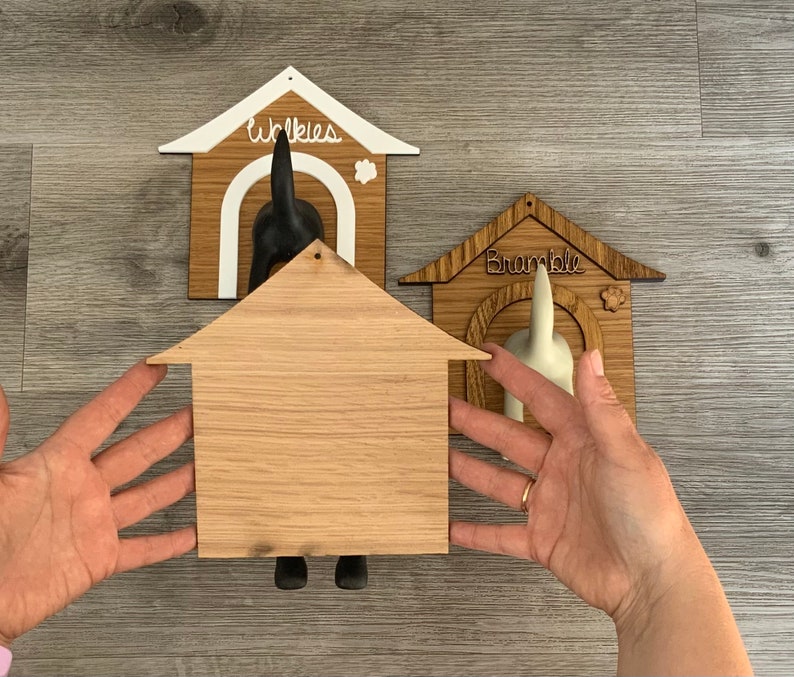 May include: Three wooden dog leash holders, each shaped like a dog house. The top house is white with the word "Winkies" written on it. The middle house is unfinished wood. The bottom house is brown with the word "Bramble" written on it.