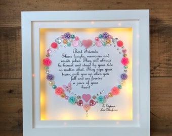 May include: A white framed heart-shaped shadow box with a light inside. The heart is decorated with colorful flowers, butterflies, and rhinestones. The text inside the heart reads "Best Friends Share laughs, memories and inside jokes. They will always be honest and stand by your side no matter what. They wipe your tears, pick you up when you fall and are forever a piece of your heart" and "To Stephanie Love Philaigh".