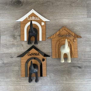 May include: Three wooden dog house shaped coat hooks with black and white dog silhouettes. The hooks are labeled "Walkies", "Bramble", and "Goose".