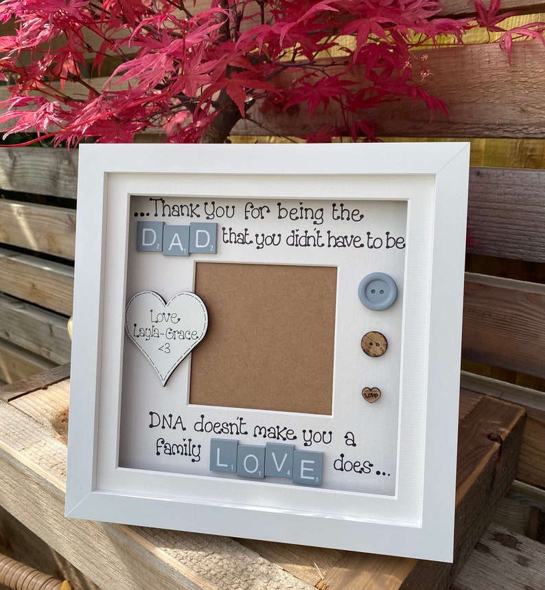 Pu&ograve; includere: Cornice per foto bianca con sfondo grigio e un'apertura per foto. La cornice contiene un messaggio che dice "...Grazie per essere il PAP&Agrave;, che non dovevi essere. Amore Layla-Grace <3. Il DNA non ti rende una famiglia, l'AMORE s&igrave;..."